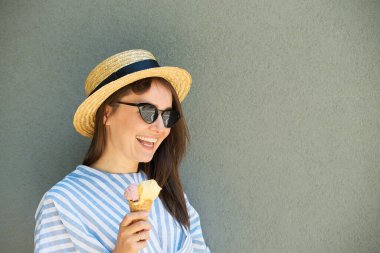 Hasır şapkalı kız dondurma yiyor Gri duvarın yanında