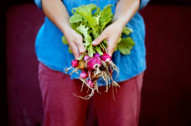 Mavi kot gömlekli kadın kamerada taze turp gösteriyor.