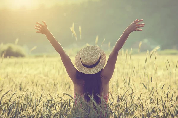 Buğday tarlasının ortasında hasır şapkalı genç kadın yazın tadını çıkarıyor. 