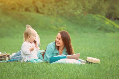 Annem parkta çimlerin üzerinde yatan bebek için kitap okuyor. Yüksek kalite fotoğraf