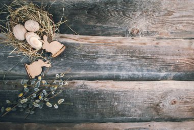 Ahşap arka planda saman ve sepetteki ahşap yumurtalarla Paskalya dekorasyonu.