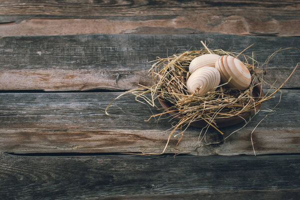 Easter decoration with wooden eggs in basket and straw on wooden background