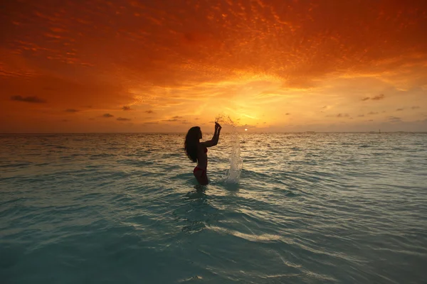 Kobieta rozpryskiwania się w morze na zachód słońca — Zdjęcie stockowe