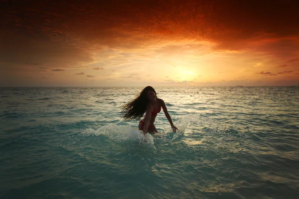 Mujer salpicando en el mar al atardecer Imagen De Stock