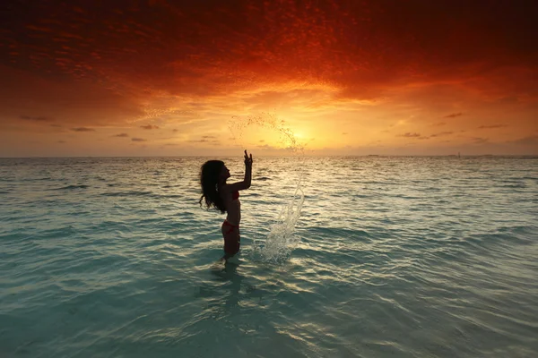 Femme éclaboussant en mer au coucher du soleil — Photo