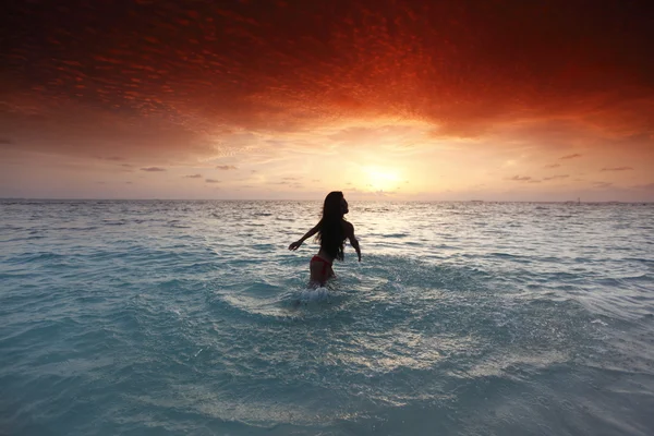 Frau planscht bei Sonnenuntergang im Meer — Stockfoto