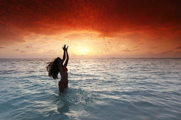 Frau planscht bei Sonnenuntergang im Meer — Stockfoto