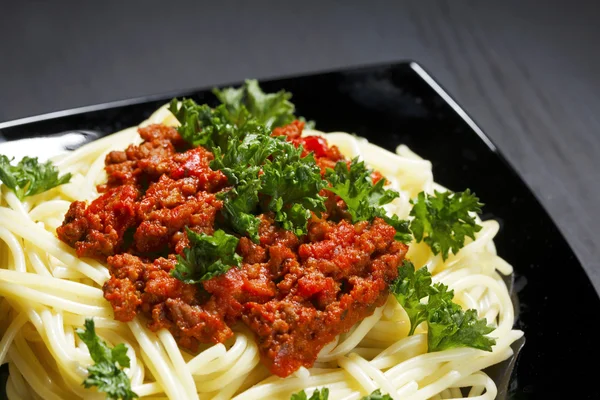Spaghetti bolognese in black plate — Stock Photo, Image