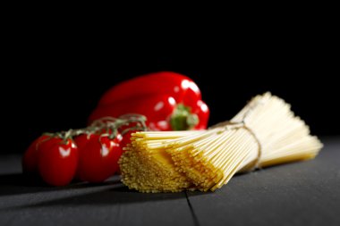 Raw pasta and vegetables on black table clipart