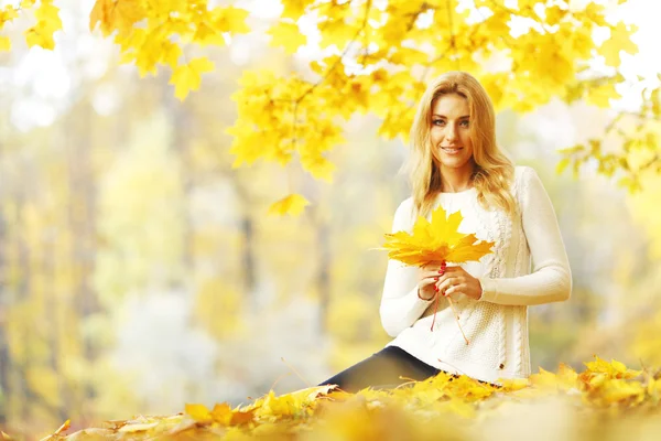 Mujer sentada sobre hojas de otoño — Foto de Stock