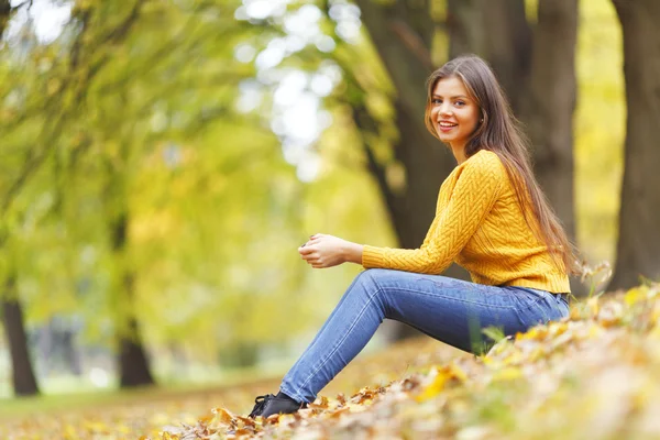 Женщина сидит на осенних листьях — стоковое фото