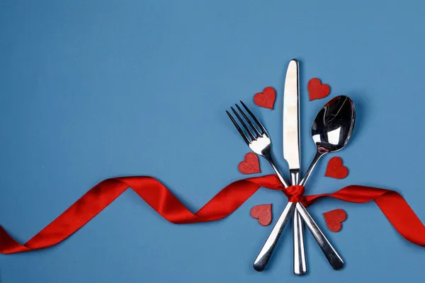用红丝带和红心系在蓝色背景下的餐具套装情人节晚餐的概念 — 图库照片