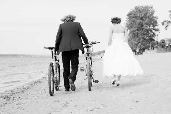 Bruid en bruidegom lopen op het strand met fietsen Rechtenvrije Stockfoto's