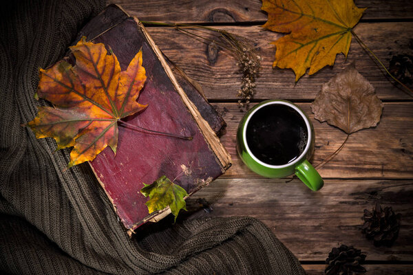 Autumn still life with a cup of coffee, fallen leaves and sweater on wooden background