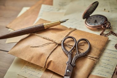 Ahşap bir masa, eski saat, kağıtlar, mektuplar, zarflar ve makas üzerine antika yazma aletleri.