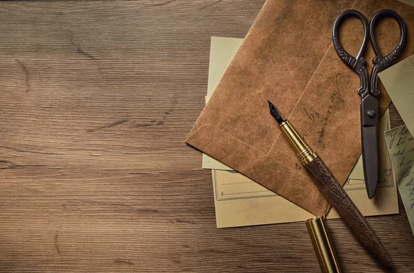 Vintage writing utensils on a wooden table, old watch, papers, letters, envelopes and scissors