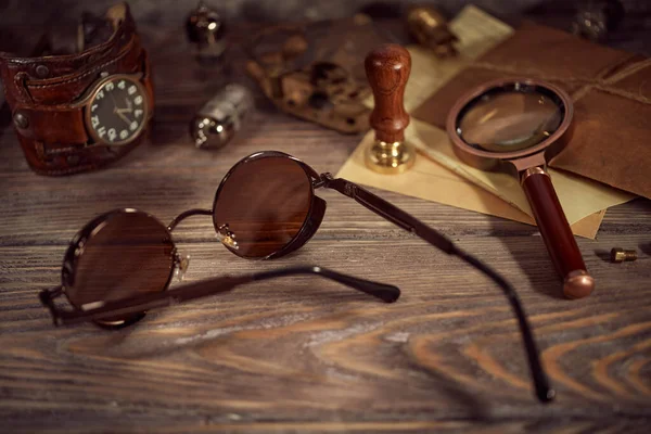 Steampunk still life - old vintage objects on a wooden background. Leather wrist watch, dark glasses, old tube lamps, magnifying glass, gears