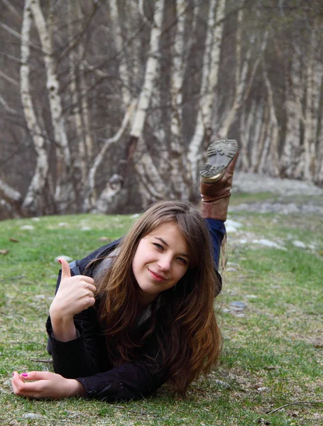 Jovem menina bonita deitada na grama e mostra OK sinal de mão — Fotografia de Stock