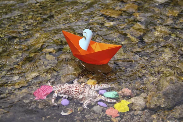 Orangefarbenes Papierboot schwimmt im Wasser auf dem Grund bunter Muscheln — Stockfoto