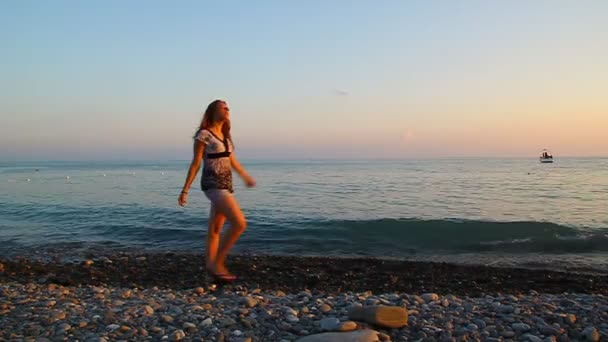 Junges schönes Mädchen, das am Strand bei Sonnenuntergang läuft und sich dreht — Stockvideo