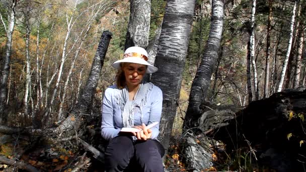 帽子坐在一棵树下，读一本书的女人 — 图库视频影像