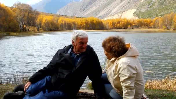 Feliz pareja de ancianos caminando a lo largo de la orilla del lago, sonriendo, hablando — Vídeos de Stock