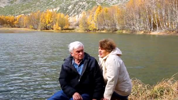 Feliz pareja de ancianos sentados y hablando en el lago — Vídeo de stock