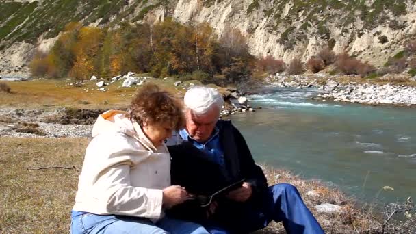 Gelukkig oudere man en vrouw zittend op de oever van het meer en pat elkaar op het hoofd — Stockvideo