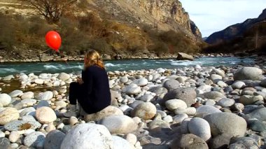 kadın kırmızı jel balon ile bir rock nehir kenarında oturur
