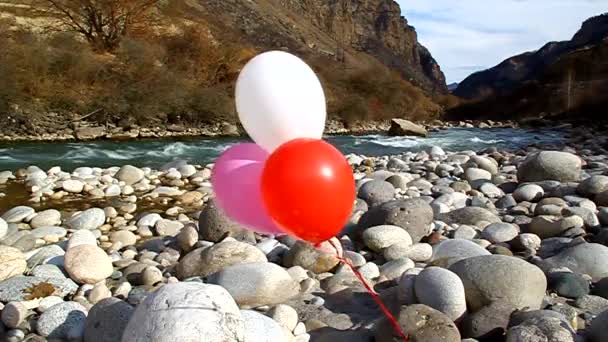 Drie helium ballonnen zijn gevlogen op de rotsen door de rivier — Stockvideo