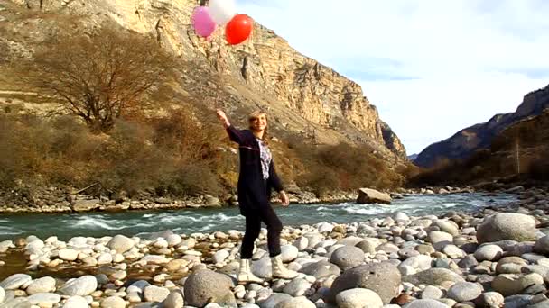 Щаслива жінка з повітряними кулями, що йдуть на березі річки — стокове відео