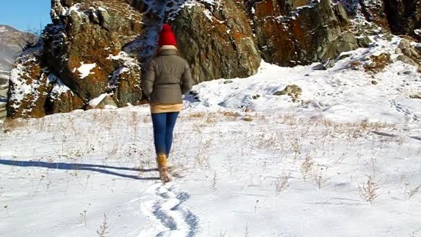 Jovem garota atravessa a neve para a rocha — Vídeo de Stock