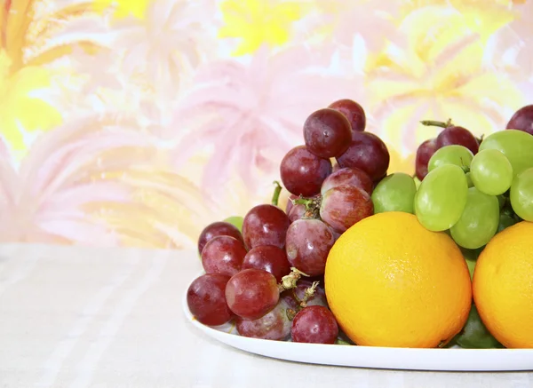 Skålen med äpplen, vindruvor och apelsiner på abstrakt färgade backgro — Stockfoto