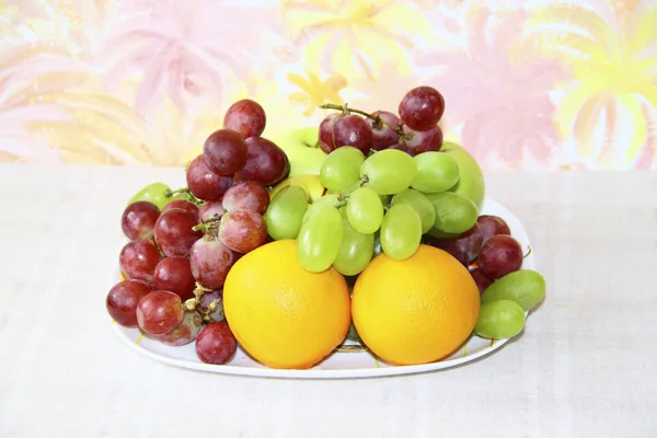 Plato con manzanas, uvas y naranjas sobre fondo de color abstracto — Foto de Stock