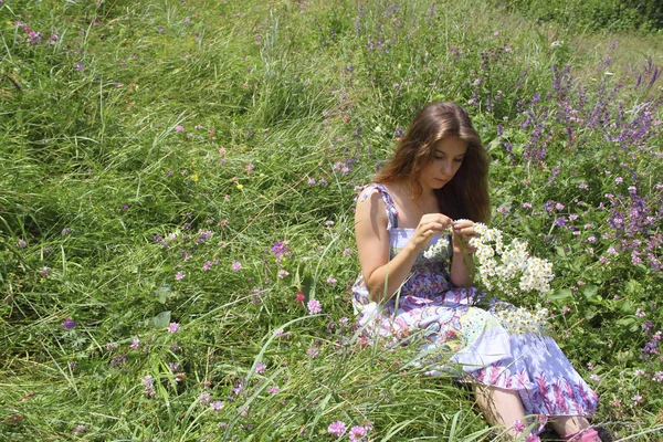 Menina em sundress sentado em um prado verde com um buquê — Fotografia de Stock