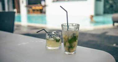 Tatil köyünün kenarında mojito kokteyli. Lüks tatil kavramı. Açık havuz arka planı, rahat eski moda renkli yakın çekim. Bulanık otel havuzuyla rahatla