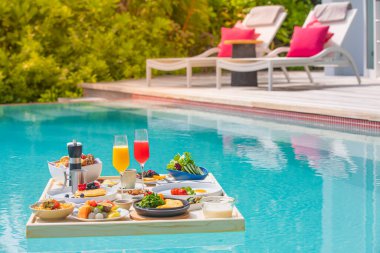 Breakfast in swimming pool, floating breakfast in luxurious tropical resort. Table relaxing on calm pool water, healthy breakfast and fruit plate by resort pool. Tropical couple beach luxury lifestyle