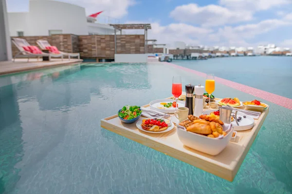 Breakfast in swimming pool, floating breakfast in luxurious tropical resort. Table relaxing on calm pool water, healthy breakfast and fruit plate by resort pool. Tropical couple beach luxury lifestyle