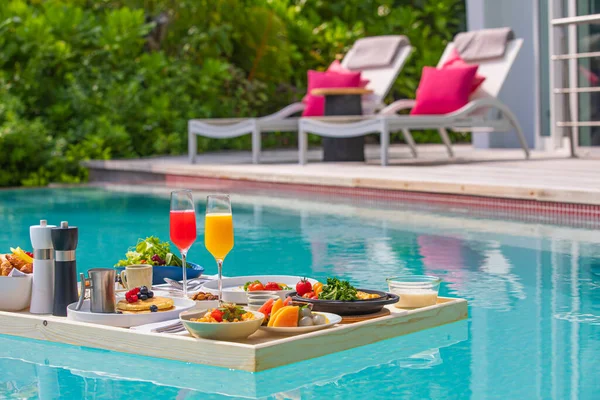 Breakfast in swimming pool, floating breakfast in luxurious tropical resort. Table relaxing on calm pool water, healthy breakfast and fruit plate by resort pool. Tropical couple beach luxury lifestyle