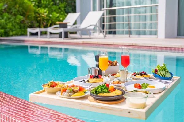 Breakfast in swimming pool, floating breakfast in luxurious tropical resort. Table relaxing on calm pool water, healthy breakfast and fruit plate by resort pool. Tropical couple beach luxury lifestyle