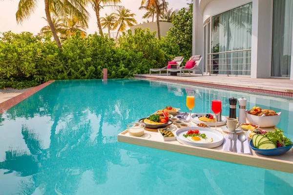 Breakfast in swimming pool, floating breakfast in luxurious tropical resort. Table relaxing on calm pool water, healthy breakfast and fruit plate by resort pool. Tropical couple beach luxury lifestyle