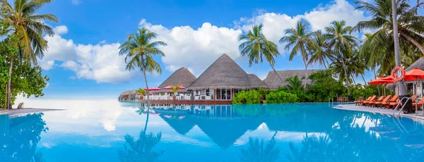 Outdoor tourism landscape. Luxurious beach resort with swimming pool and beach chairs or loungers under umbrellas with palm trees and blue sky. Exotic summer travel and vacation background concept