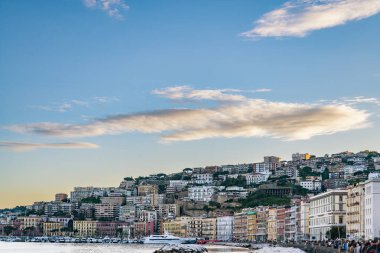 Kasvetli bir bahar akşamında Napoli körfezinde yüzen balıkçı tekneleri. Napoli rıhtımı, arkasında Napoli tepeleri ve binaları var. İtalya.