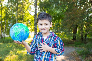 Neşeli bir çocuk bir elinde küre tutuyor. Doğanın arka planına karşı bir okul çocuğunun portresi.