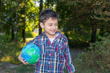 Ormanın arka planında küresi olan gülümseyen bir çocuk.