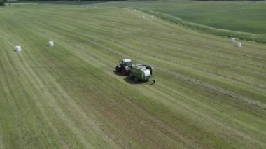 Plunge İlçesi, Litvanya - 12 Haziran 2022: Traktörün beyaz film ile nasıl balya yaptığını gösteren hava manzarası