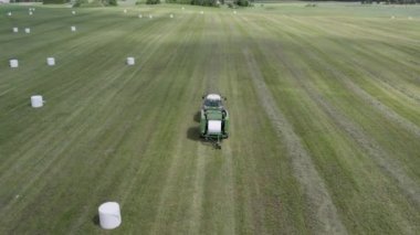 Plunge İlçesi, Litvanya - 12 Haziran 2022: Traktörün beyaz film ile nasıl balya yaptığını gösteren hava manzarası