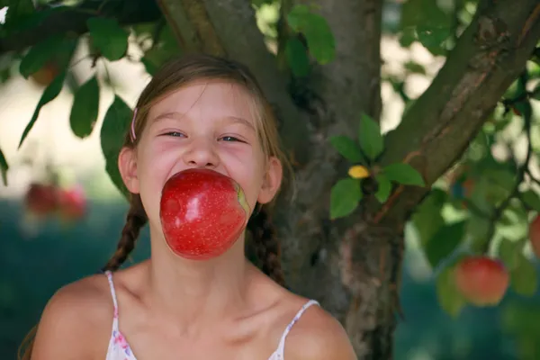 Flicka bita i ett äpple under ett äppelträd — Stockfoto