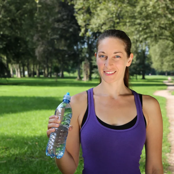 Donna sportiva che tiene in mano la bottiglia d'acqua durante la corsa — Foto Stock