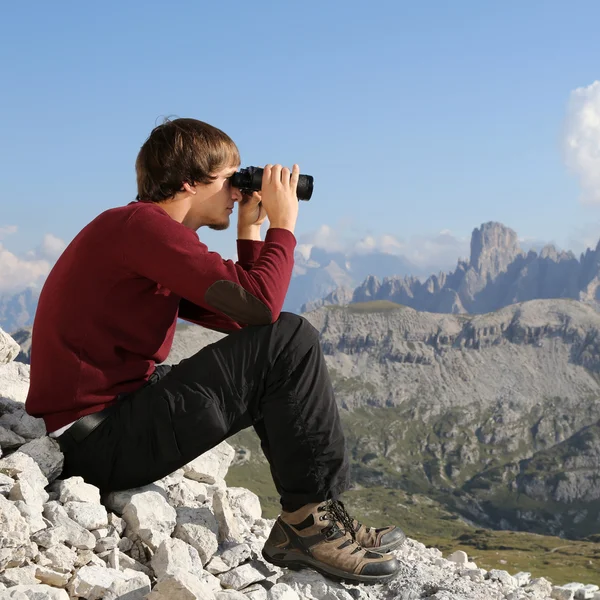 Young man looking through binoculars in the mountains — Stock Photo, Image